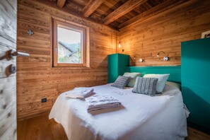 Ein Schlafzimmer einer Holzhütte mit einem Bett, Kissen, einem Fenster und einer wandmontierten Lampe.