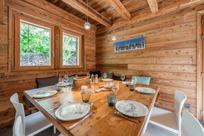 A wooden interior with a dining table set for four, surrounded by white chairs.