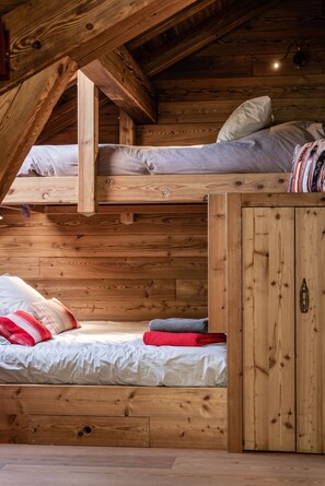 A wooden cabin with a loft-style bedroom, a bunk bed, and a wooden wardrobe.