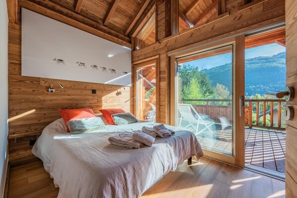 A wooden cabin bedroom with a bed, pillows, and a large window.
