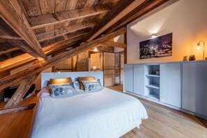 A bedroom with a sloped ceiling, a bed with pillows, a wardrobe, and a painting on the wall.