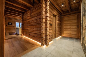 A log cabin interior with a wooden wall, a door, and a tiled floor.