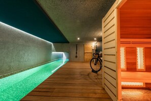 A spa area with a wooden floor, a green-lit pool, and a sauna.