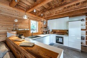 A modern kitchen with wooden beams, white cabinetry, a built-in oven, and a large window. - Chalet Twin - Piscine Privée et Sauna (La Salle-les-Alpes)