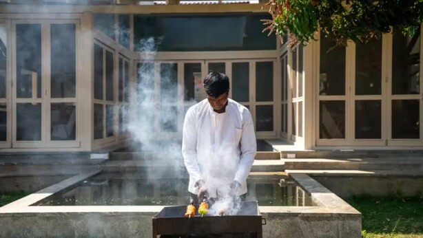 Una persona cucina all'aperto con effetto fumo, di fronte a un edificio con ampie finestre.