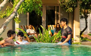 A pool area with people relaxing and a building in the background. - Serene Luxury Villa with Infinity Pool & Garden (Ramanagara)