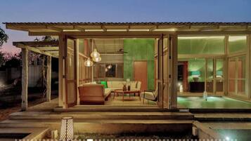 Ein modernes Haus mit Glasfassade, einem Pool und einer Terrasse mit Möbeln.