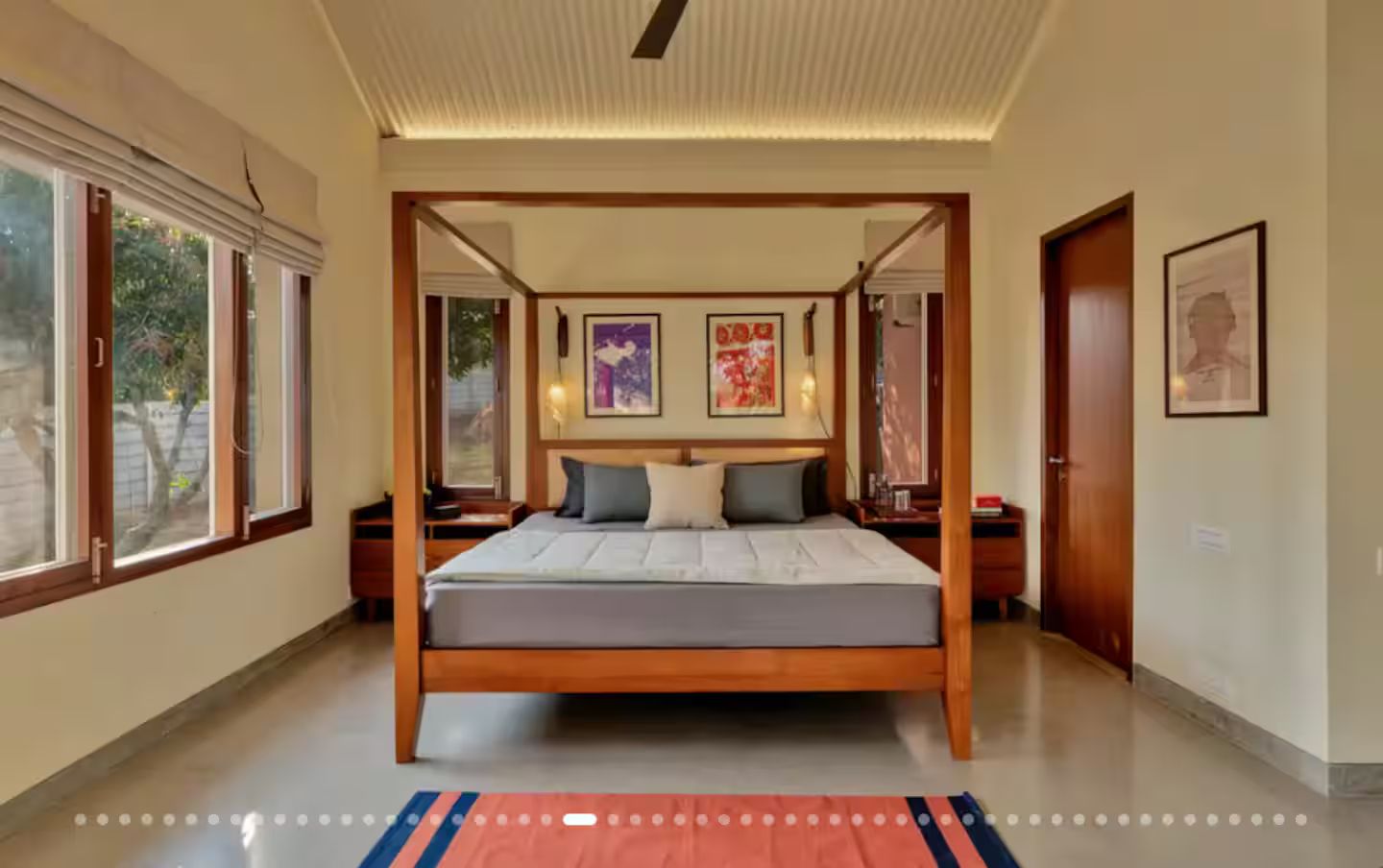 Una cama con dosel de madera, un colchón plano y un tapete a rayas azul y rojo.