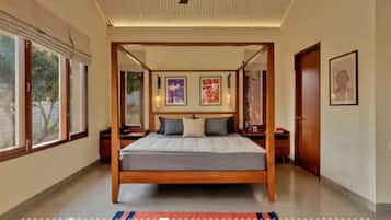 A four-poster bed with a wooden frame, a flat mattress, and a red and blue striped rug.