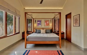A four-poster bed with a wooden frame, a flat mattress, and a red and blue striped rug.