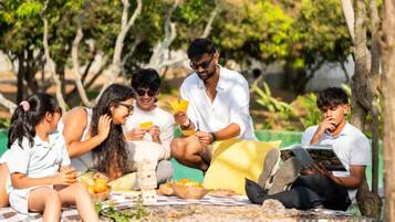A group of people sitting on a checkered blanket outdoors, some eating and others reading.