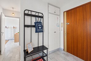 Une chambre d’hôtel avec une porte en bois, un présentoir en métal noir sur lequel sont posés une serviette et un menu, et un mur blanc orné d’un panneau « interdiction de fumer ».