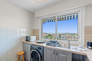 A modern kitchen with a built-in washing machine, a microwave, and a sink. - Le Panoramic Lérins - 2km de la Plage (Antibes)