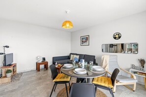 A modern living room with a dining area, a sofa, a TV, and a ceiling light. - Le Panoramic Lérins - 2km de la Plage (Antibes)