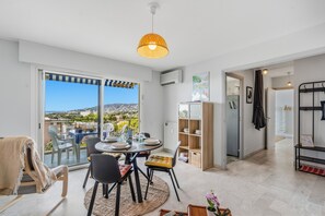 A dining area with a view of the city, a kitchen with a radiator, and a hallway leading to a bedroom. - Le Panoramic Lérins - 2km de la Plage (Antibes)