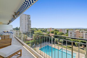 Un balcon avec une piscine, donnant sur un quartier résidentiel avec des immeubles et de la verdure.