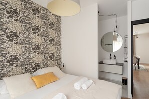 Ein Hotelzimmer mit einem Bett, einem großen Spiegel, einer runden Leuchte und einem durchgegangenen Badezimmereingang.