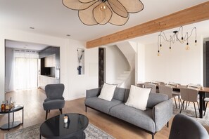 Ein modernes Wohnzimmer mit einem grauen Sofa, einem runden Couchtisch und einem Essbereich mit einem Holztisch und Stühlen.