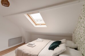 A bedroom with a skylight, a bed with white linens, a green pillow, and a wall with a leaf pattern. - Maison Nova - charmant appt avec parking priv é (Rennes)