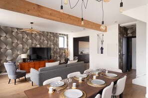 A modern living room with a flat-screen TV, grey sofa, wooden dining table set with plates and glasses, and a patterned wall. - Maison Nova - charmant appt avec parking privé (Rennes)