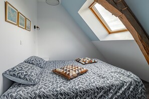 A bedroom with a sloped ceiling, a skylight, a bed with patterned bedding, and wall-mounted artwork. - La Saulnerie - appt climatisé avec jardin (Martizay)