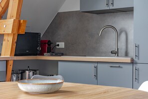A modern kitchen with a grey countertop, a stainless steel sink, and a wooden table with a ceramic bowl.