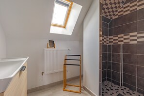 A bathroom with a skylight, a radiator, a towel rack, and a shower with patterned tiles.