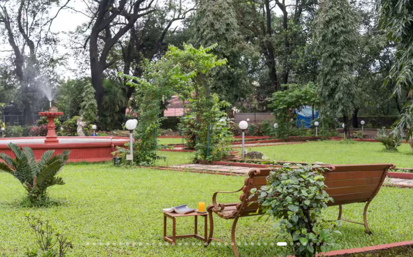 A park with a bench, a small table with a book and a cup, and a fountain.