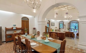 Un'ampia sala da pranzo con un lungo tavolo, sedie di legno e un lampadario.