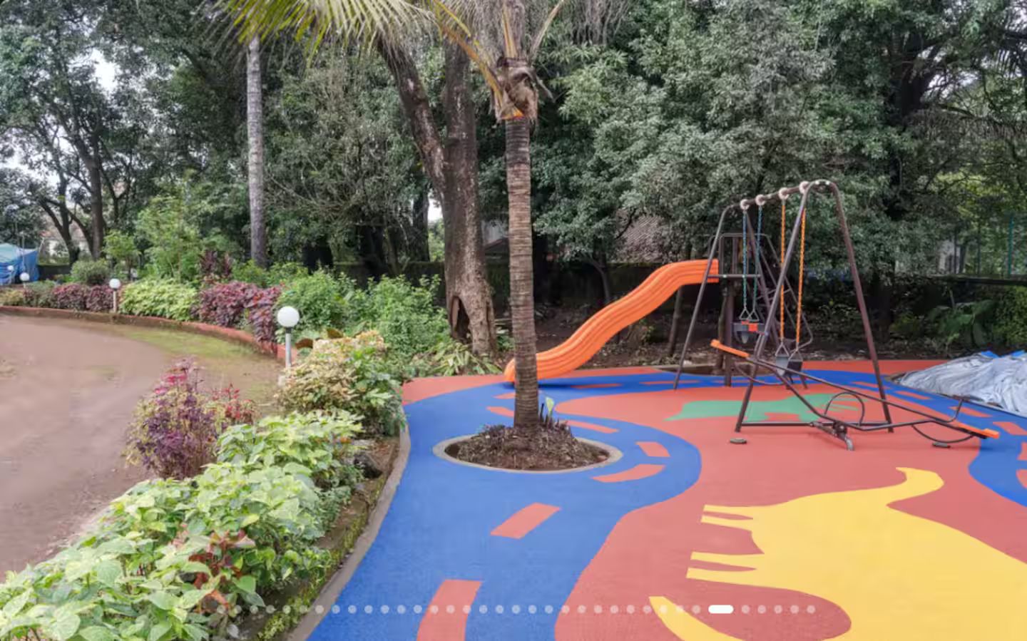 A playground with a slide and swings, surrounded by trees and plants.