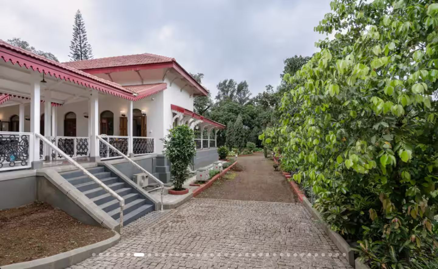 A building with a red-tiled roof, a covered porch with a staircase, and a paved pathway leading to a garden area.