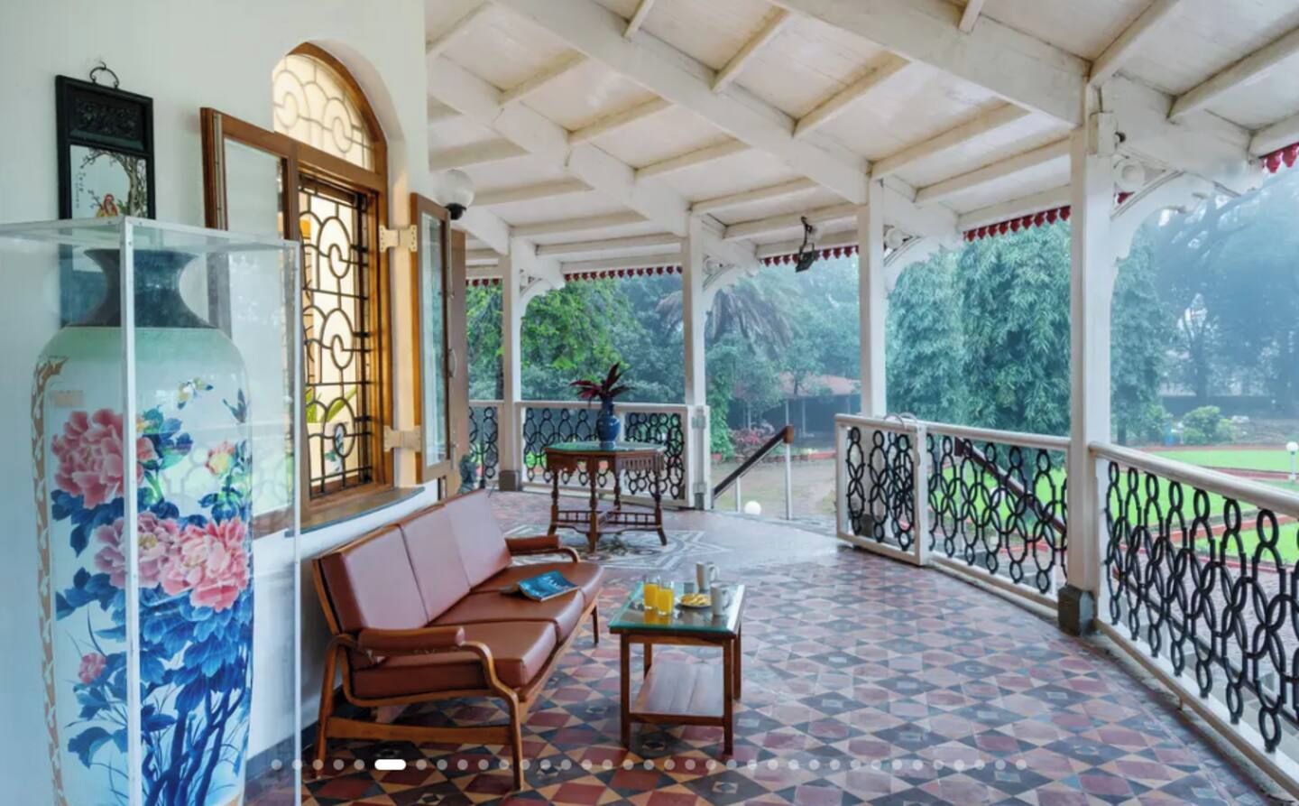 A covered porch with a patterned floor, a sofa, a table with a glass top, and a view of greenery outside.