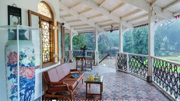 A covered porch with a patterned floor, a sofa, a table with a glass top, and a view of greenery outside.