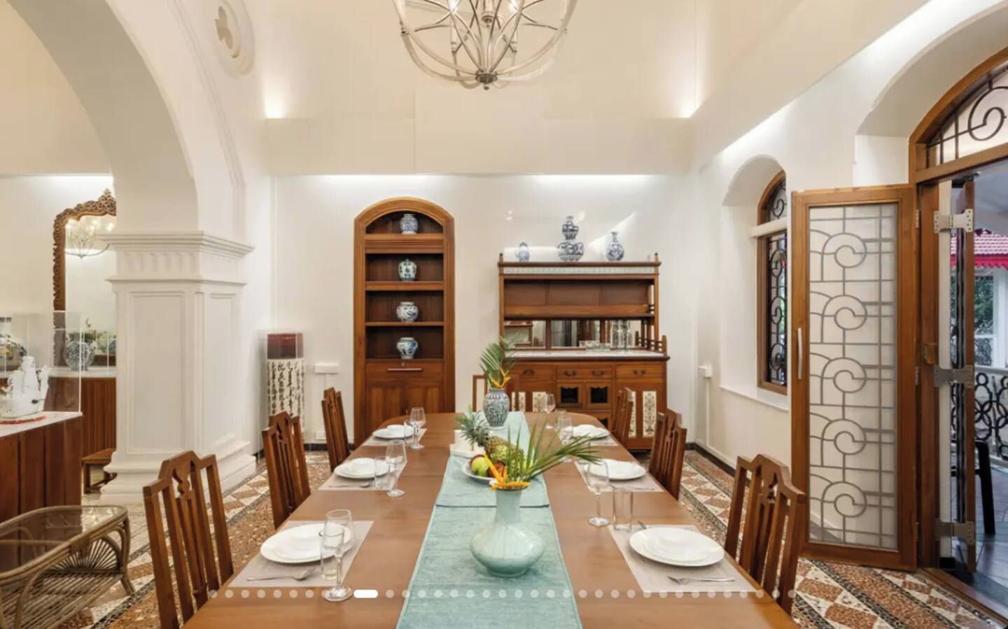 Un comedor con una mesa larga, sillas, un florero central y una estantería al fondo.