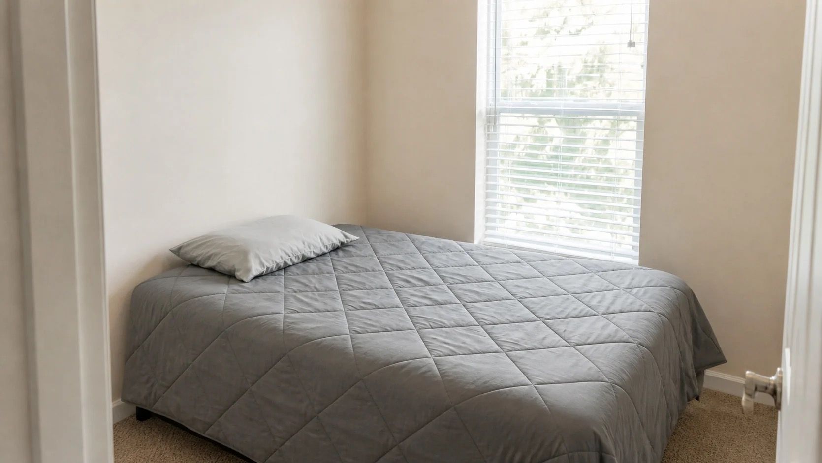 Un dormitorio con una cama, una ventana con persianas y una puerta.