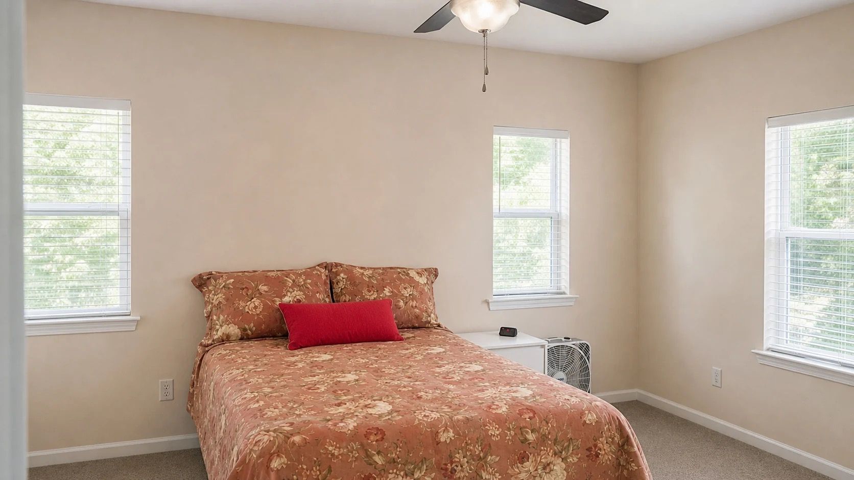 A bedroom with a bed, two windows, a ceiling fan, and a nightstand.