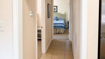 Un couloir menant à une chambre à coucher, où se trouvent un lit, une porte et une poubelle.