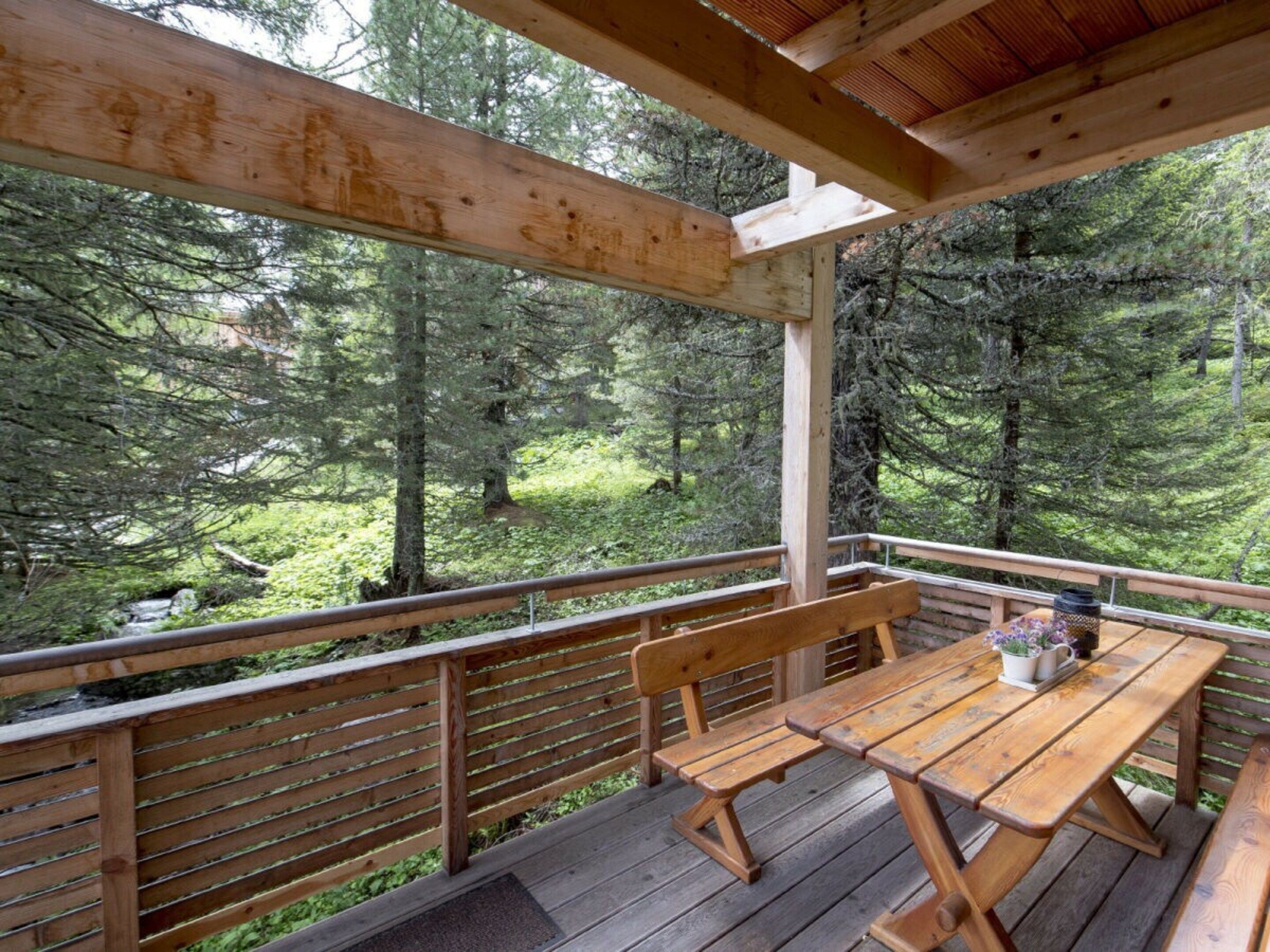 A wooden deck with a picnic table and benches, surrounded by a forested area. - Cabin in Turrach With Sauna and Balcony (Stadl-Predlitz)