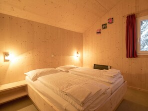 A room with a wooden ceiling, a bed with white bedding, a nightstand, a wall-mounted light, and a window with a curtain. - Cabin in Turrach With Sauna and Balcony (Stadl-Predlitz)
