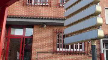 Un bâtiment en briques rouges, avec une enseigne, une porte rouge et un pot de fleurs.