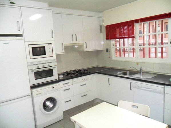 A compact kitchen with a washing machine, a stove, a microwave, and a sink.