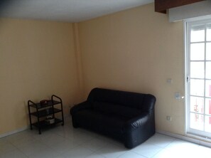Una habitación con un sofá de cuero negro, un estante metálico pequeño y un cerramiento de vidrio corredero que da a un espacio exterior.