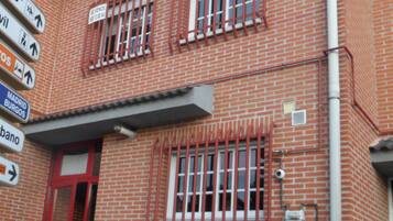 A red brick building with a red door and windows, a sign with directions, and a small plant in front.