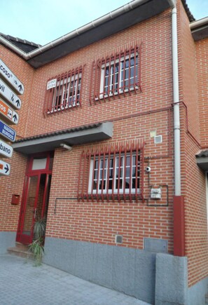 Un edificio de ladrillo rojo con puerta y ventanas rojas, una señal con indicaciones y una planta pequeña en el frente.