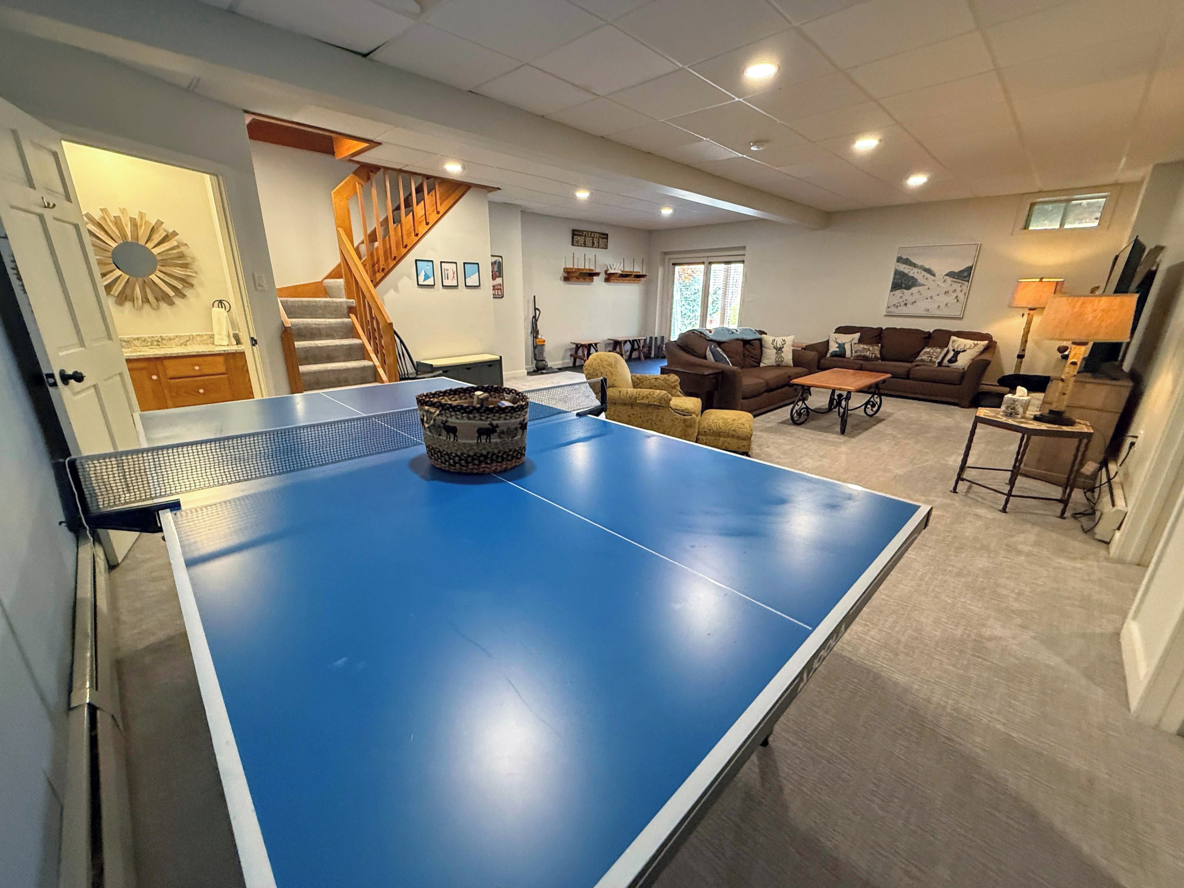 A living room with a ping pong table, a staircase, and a sofa.