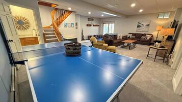 A living room with a ping pong table, a staircase, and a sofa.