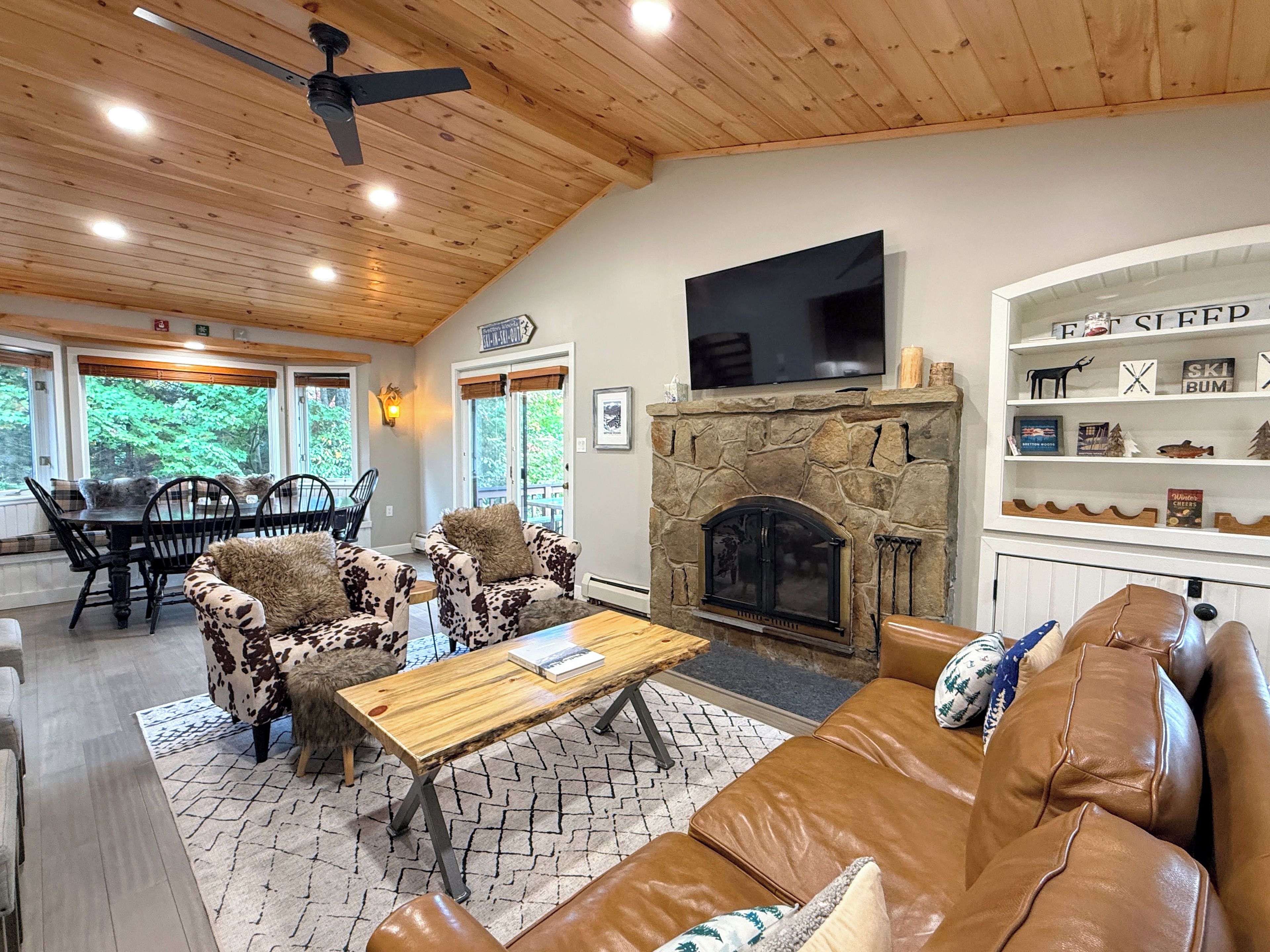 A cozy living room with a stone fireplace, leather sofa, and a television mounted above it.