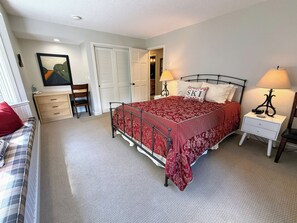 Une chambre à coucher comprenant un lit, deux tables de chevet, une commode, une chaise, une coiffeuse et une porte donnant sur une autre pièce.