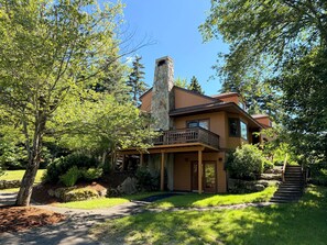 A two-story house with a stone chimney, a balcony, and a stone staircase leading to the entrance.