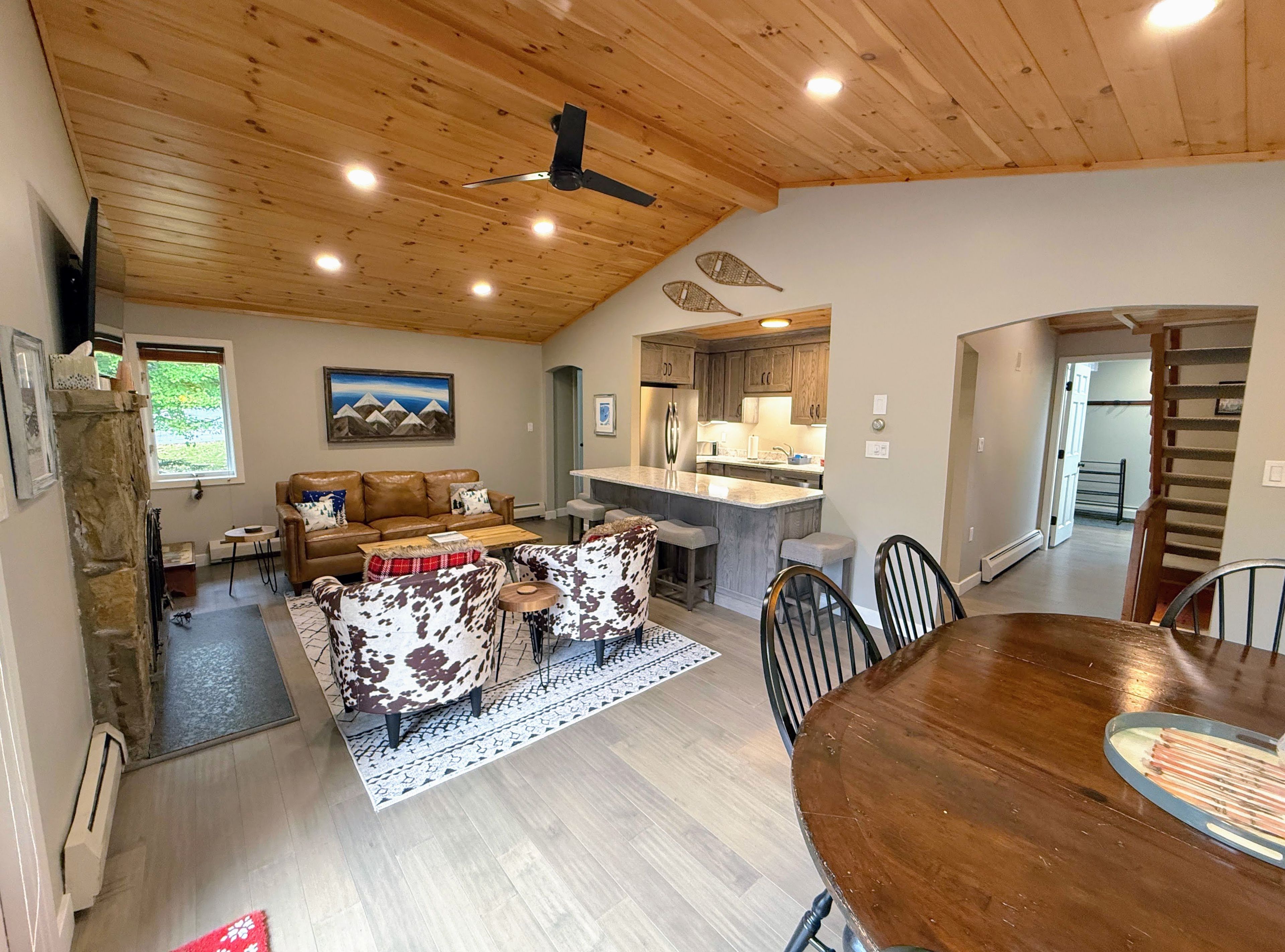 A cozy living area with a wooden ceiling, a dining table, and a kitchen in the background.